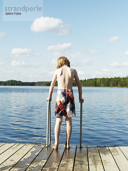 Junge steht auf einem Steg und will ins Wasser gehen
