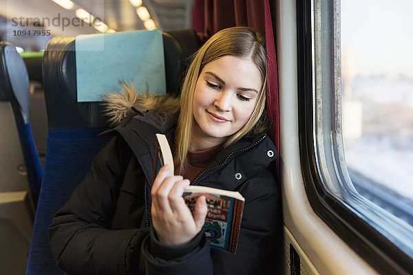 Junge Frau liest ein Buch im Zug