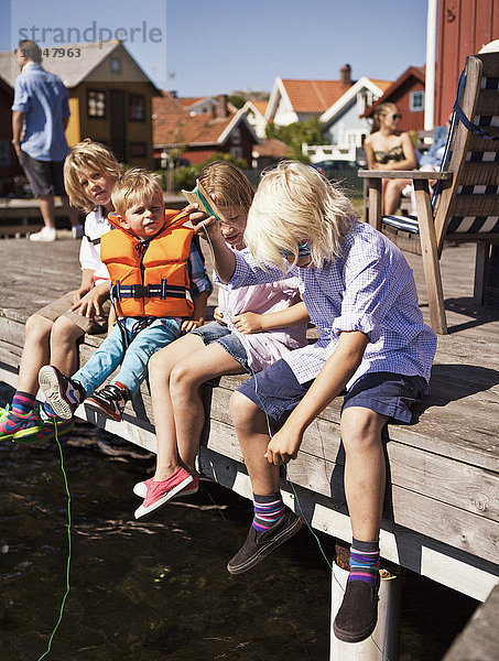 Kinder sitzen auf dem Steg und angeln