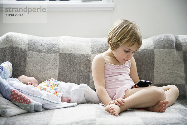 Mädchen sitzt mit kleinem Bruder auf dem Sofa und benutzt ein Mobiltelefon