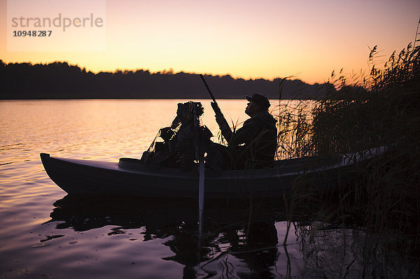 Jäger im Boot auf dem See in der Abenddämmerung