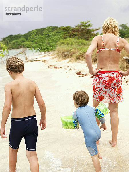 Mutter mit zwei Söhnen spazieren am Strand