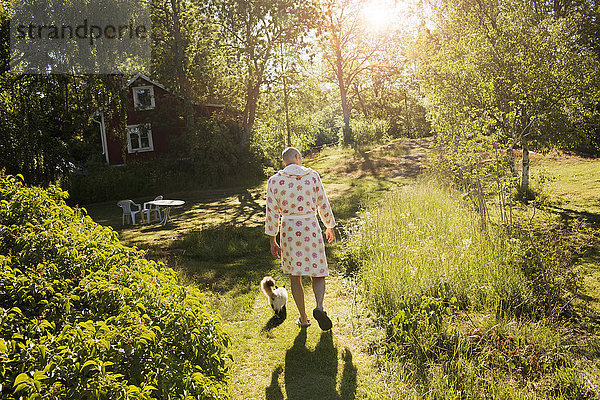 Älterer Mann im Morgenmantel geht im Garten mit Katze spazieren