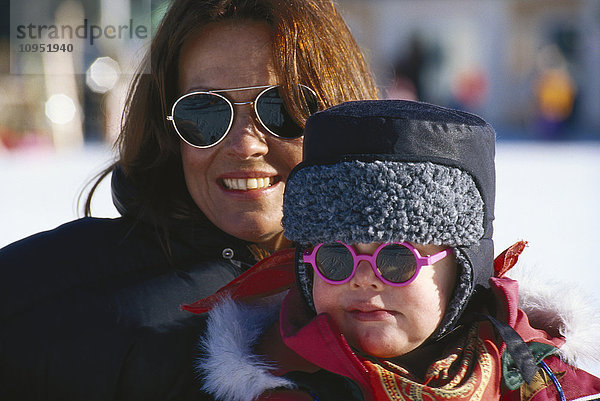 Porträt einer lächelnden Frau mit Sonnenbrille und einem Kind.