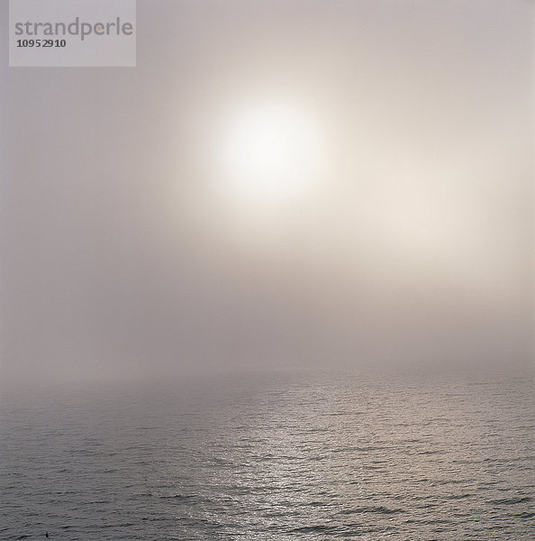 Die Sonne scheint durch den Nebel über dem Meer
