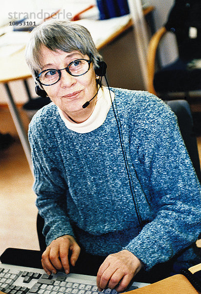 Ältere Frau mit Headset und Computer im Büro