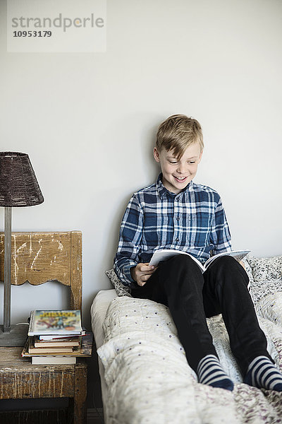 Lächelnder Junge beim Lesen auf dem Bett