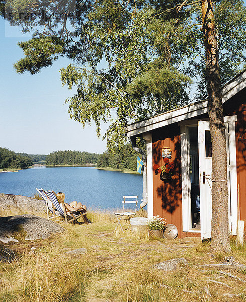 Eine Frau sitzt vor einem roten Häuschen am Meer  Schweden.