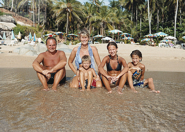 Eine Familie sitzt am Strand in der Sonne am Wasser.