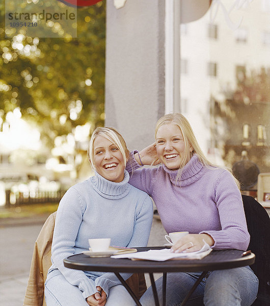 Lachende Frauen  die am Tisch sitzen und Kaffee trinken.