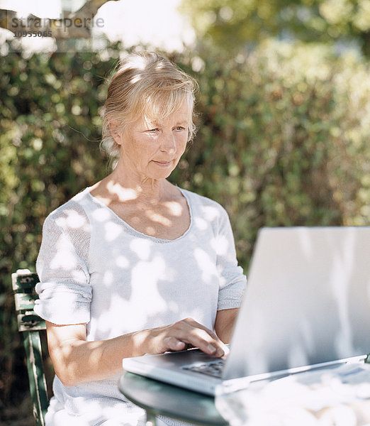 Ältere Frau benutzt Laptop im Garten