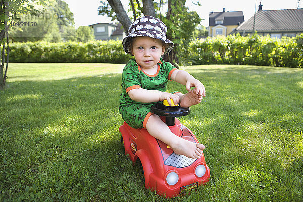 Junge auf einem Spielzeugauto in einem Garten  Schweden.