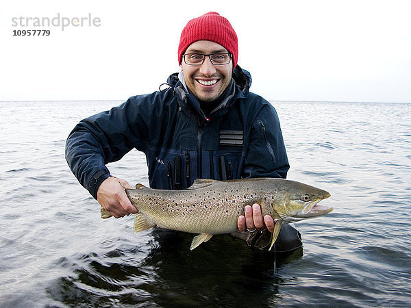 Mann im Wasser stehend mit einem frisch gefangenen Fisch  Schweden.