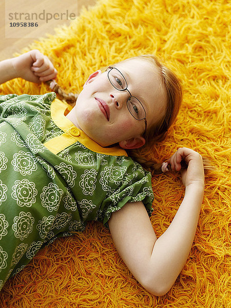 Rothaariges Mädchen auf einem gelben Teppich liegend  Schweden.