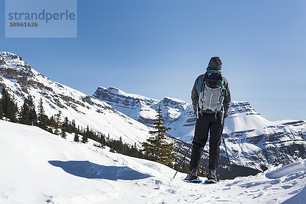 Schneeschuhwanderin mit Blick auf eine schneebedeckte Bergkette und blauen Himmel; Banff  Alberta  Kanada'.