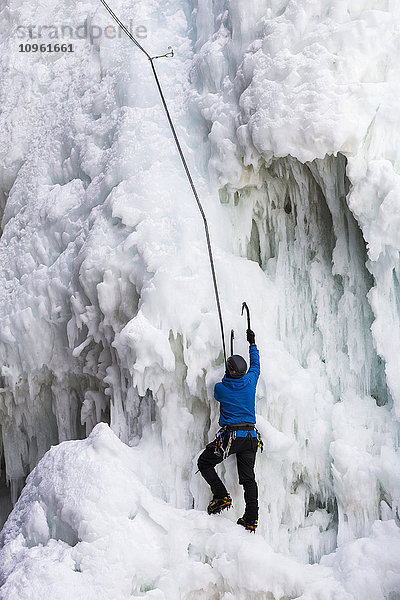 Eiskletterer mit Eispickel klettert an gefrorener Felswand; Banff  Alberta  Kanada'.
