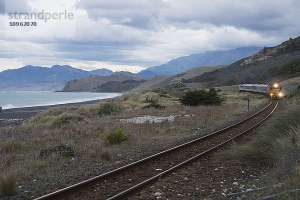 Annähernder Zug mit malerischer Meeres- und Bergkulisse an der Ostküste der Südinsel Neuseelands; Neuseeland'.