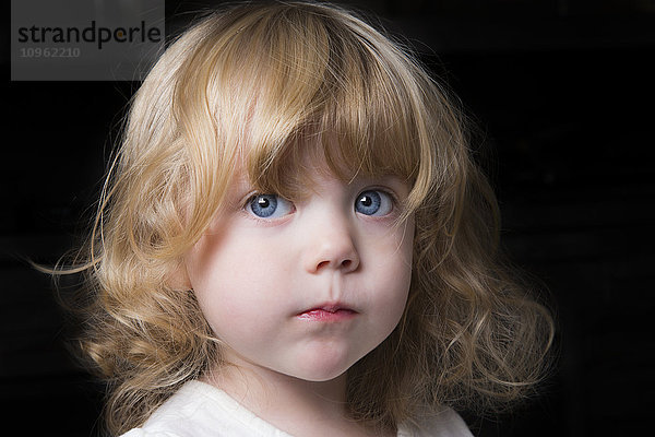 Porträt eines schönen jungen Mädchens mit großen blauen Augen und lockigem blondem Haar auf schwarzem Hintergrund; Spruce Grove  Alberta  Kanada'.