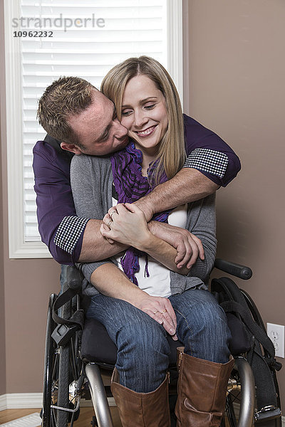 Ehemann umarmt seine behinderte Frau in ihrem Haus; Spruce Grove  Alberta  Kanada'.
