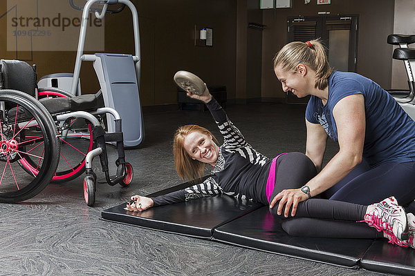Physiotherapeutin  die einer jungen Frau mit einer Rückenmarksverletzung bei der Ausführung von Oberkörper-Windschutzscheibenwischern und gewichteten schrägen Drehungen hilft; Edmonton  Alberta  Kanada .