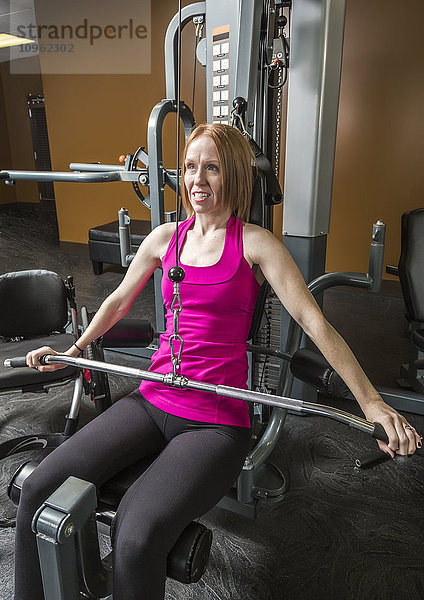 Junge behinderte Frau benutzt eine Schulterpresse  um sich nach einer Wirbelsäulenverletzung zu rehabilitieren; Edmonton  Alberta  Kanada'.