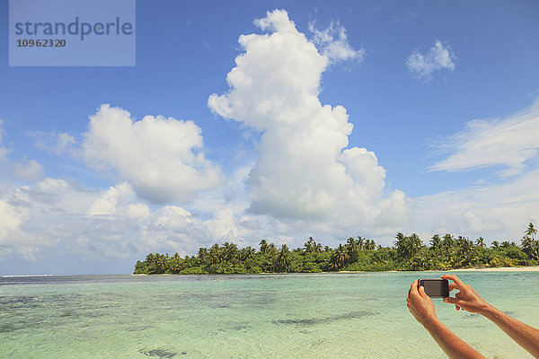 Frau fotografiert ein Atoll mit einem Smartphone; Insel Medahutthaa  Nord-Huvadhoo-Atoll  südliche Malediven'.