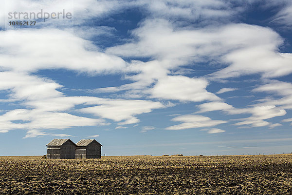 Zwei Holzhütten in einem Stoppelfeld mit dramatischen Wolken und blauem Himmel; Alberta  Kanada'.