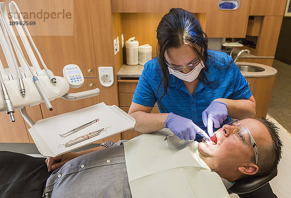 Männlicher Patient im Zahnarztstuhl während eines zahnärztlichen Eingriffs durch eine Zahnarzthelferin; Edmonton  Alberta  Kanada'.