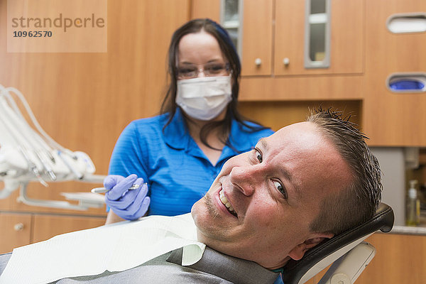 Männlicher Patient im Zahnarztstuhl während eines zahnärztlichen Eingriffs durch eine Zahnarzthelferin; Edmonton  Alberta  Kanada'.