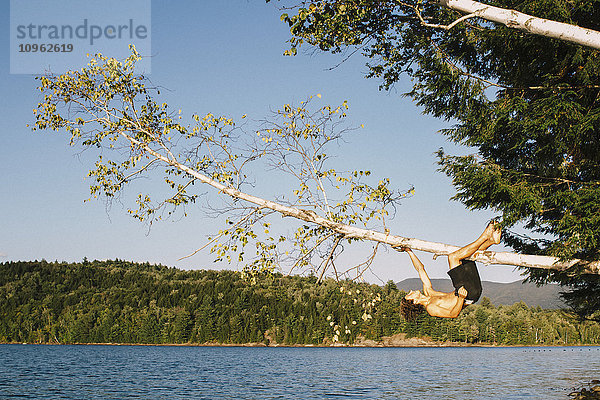 Ein junger Mann  der sich an einem Ast festhält  der über einen See ragt; Waterbury  Vermont  Vereinigte Staaten von Amerika'.