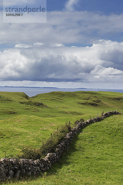 Eine Steinmauer  die sich über Grasflächen erstreckt  und ein Blick auf das Meer