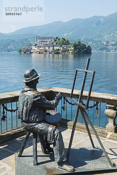 Statue eines Künstlers  der an einer Staffelei sitzt und malt  mit Blick auf die Insel San Giulio im Ortasee; Orta  Piemont  Italien'.