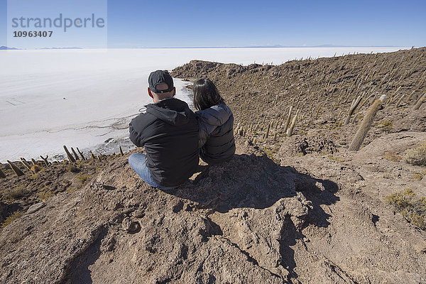 Paar sitzt auf einer Insel aus Felsen und Kakteen namens Incahuasi; Uyuni  Bolivien