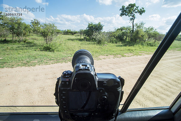 Eine Kamera am Fenster eines Fahrzeugs  das auf den Krüger-Nationalpark zeigt; Südafrika'.