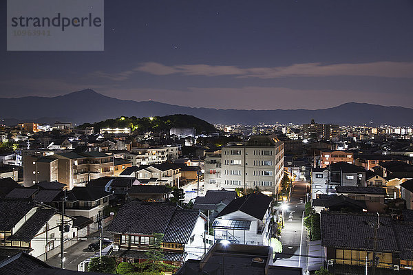 Beleuchtete Straßen und Gebäude in der Abenddämmerung  mit Silhouetten der Berge in der Ferne; Kyoto  Japan'.