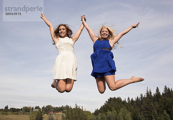 Zwei jugendliche Sportler in Kleidern  die in einem Park hoch in die Luft springen; Edmonton  Alberta  Kanada'.