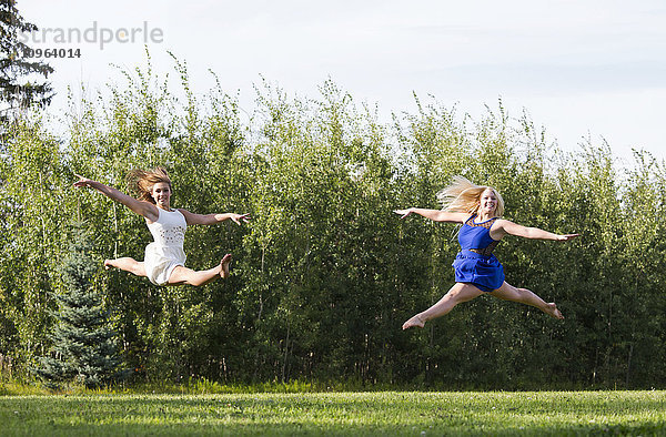 Zwei Turnerinnen üben in ihren Kleidern ihre Spagatsprünge in einem Park; Edmonton  Alberta  Kanada'.