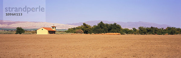 Ein brachliegendes Feld liegt im Vordergrund mit einer Landkirche  grünen Feldern und Bergen dahinter  Santa Ynez Valley; Lompoc  Kalifornien  Vereinigte Staaten von Amerika'.