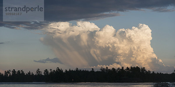 Eine im Sonnenlicht leuchtende Wolkenformation über einer Waldsilhouette und einem See; Ontario  Kanada'.