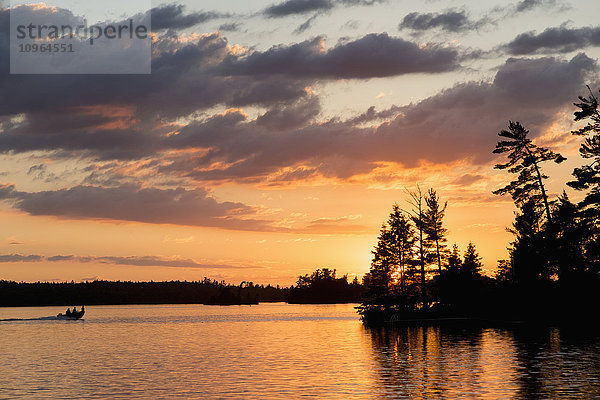 Silhouette von Menschen in einem Kanu auf einem ruhigen See bei Sonnenuntergang; Ontario  Kanada'.