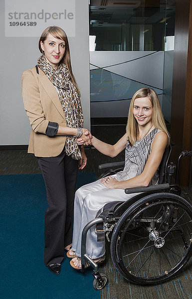Eine professionelle Geschäftsfrau schüttelt einer jungen querschnittsgelähmten Frau im Rollstuhl die Hand und posiert mit ihr; St. Albert  Alberta  Kanada'.