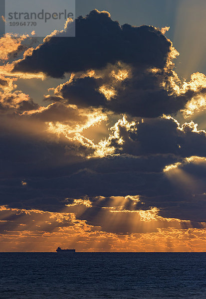 Dramatischer Himmel mit leuchtenden Wolken bei Sonnenuntergang über dem Meer und einem Schiff in der Ferne; Tarifa  Cadiz  Andalusien  Spanien'.