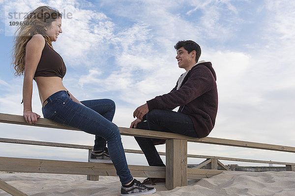 Ein junger Mann und eine Frau sitzen auf einem Holzzaun am Strand und unterhalten sich; Tarifa  Cadiz  Andalusien  Spanien'.
