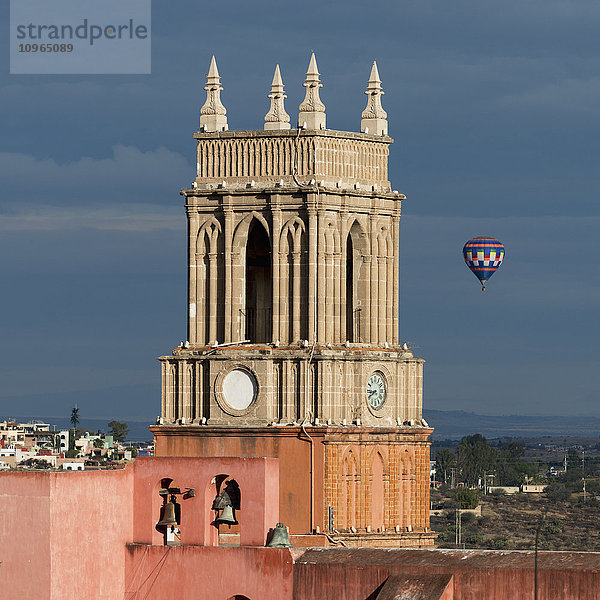 Uhrturm und Glocken der Pfarrkirche mit einer Heißluftballonfahrt in der Ferne; San Miguel de Allende  Guanajuato  Mexiko