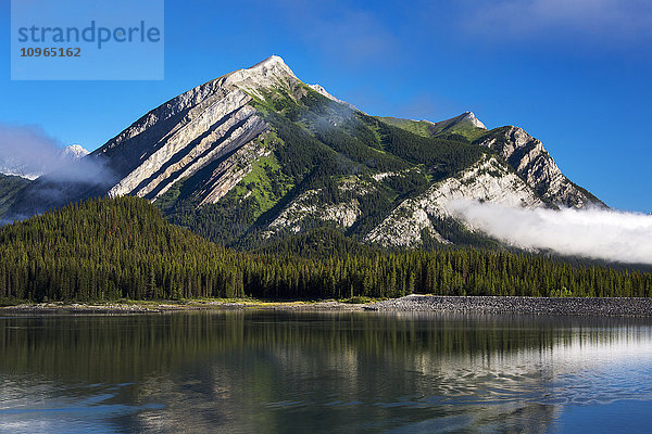 Berg  der sich in einem See mit Nebelflecken und blauem Himmel spiegelt; Kananaskis Country  Alberta  Kanada'.