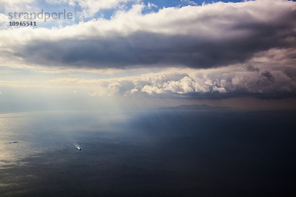 Ein einsames Boot auf dem Ägäischen Meer bei bewölktem Himmel und Fernsicht auf die Küstenlinie; Griechenland