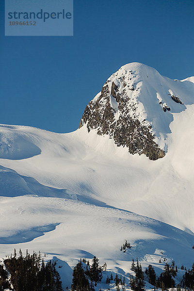 Ein felsiger Gipfel ist mit einer frischen Schneeschicht bedeckt  das späte Nachmittagslicht wirft tiefe Schatten auf die Landschaft  Kings Bay  Prince William Sound; Whittier  Süd-Zentral-Alaska  Vereinigte Staaten von Amerika'.