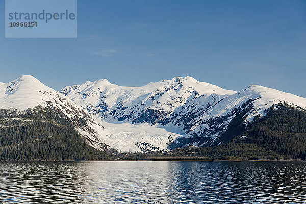 Ein Gletscher liegt im Tal der schneebedeckten Berge über Hängen mit immergrünen Bäumen in Kings Bay  Prince William Sound; Whittier  Alaska  Vereinigte Staaten von Amerika'.