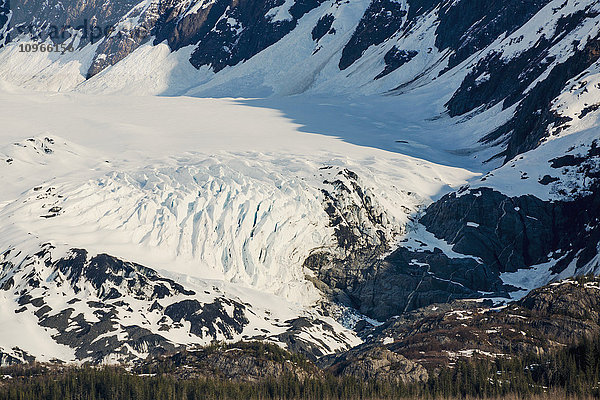 Ein Gletscher liegt im Tal der schneebedeckten Berge über Hängen mit immergrünen Bäumen in Kings Bay  Prince William Sound; Whittier  Alaska  Vereinigte Staaten von Amerika'.