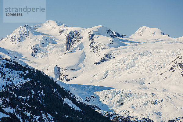 Ein Gletscher hängt in einem Tal unter zerklüfteten schneebedeckten Gipfeln in Kings Bay  Prince William Sound; Whittier  Alaska  Vereinigte Staaten von Amerika'.